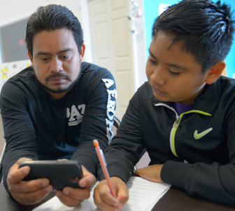 Using an app that scans an English text and translates it into Spanish, Ramon Leon helps his son with homework at the VAYLA office in eastern New Orleans.