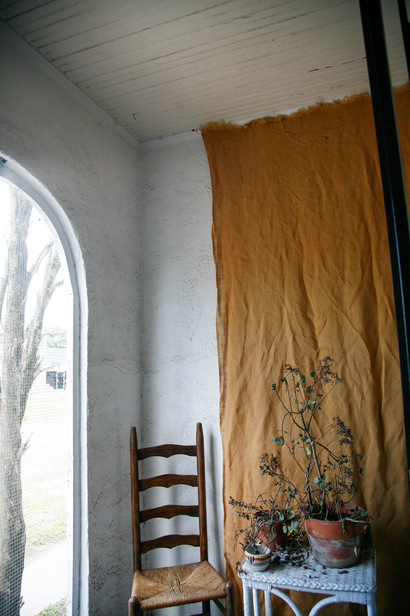 Photograph of Gus Bennett’s porch studio in New Orleans after Hurricane Katrina, with remnants of plants, furniture, and personal items that survived the storm.