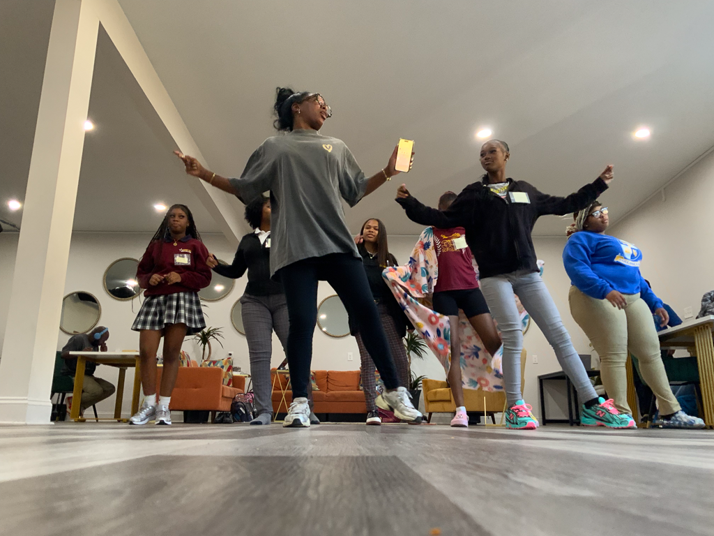 Jazz Johnson leads a dance class with Daughters Beyond Incarceration mentees, guiding a group of young women as they practice movements together in a bright studio space.
